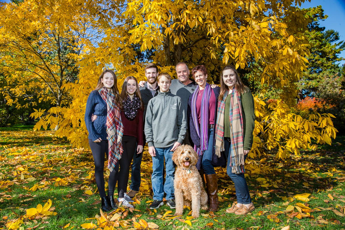 Kristen posing with her family during an outdoor photo shoot at the arboretum in autumn.