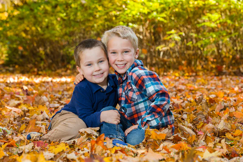 Two brothers hug each other while sitting in the leaves for a family portrait by Jeffrey Meyer