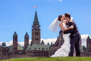 A bride and groom kiss in front of parliament hill