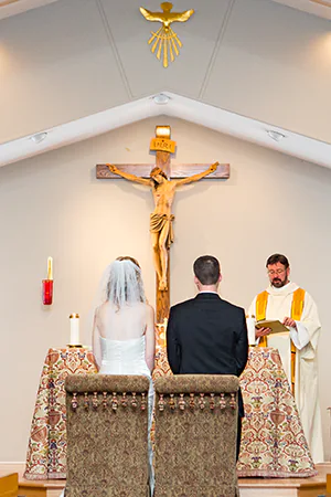 A bride and groom face their paster and a crucifix during their wedding ceremony