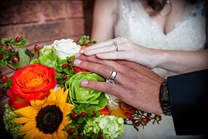 A bride and groom place their hands on a flower bouquet to profile their rings